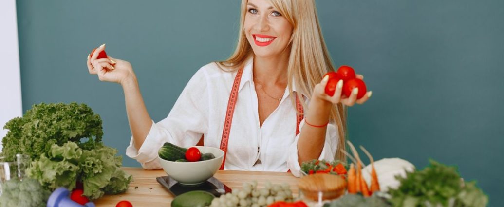 Healthy lifestyle concept with woman holding tomatoes and surrounded by fresh vegetables in a studio setting.