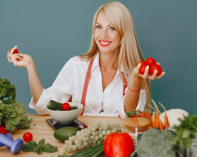 Healthy lifestyle concept with woman holding tomatoes and surrounded by fresh vegetables in a studio setting.